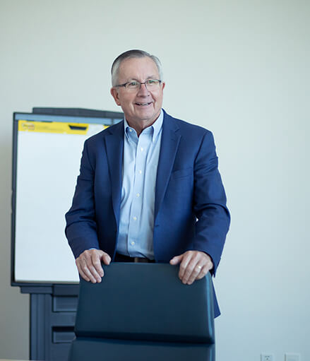 John Morris in a jacket standing with a chair